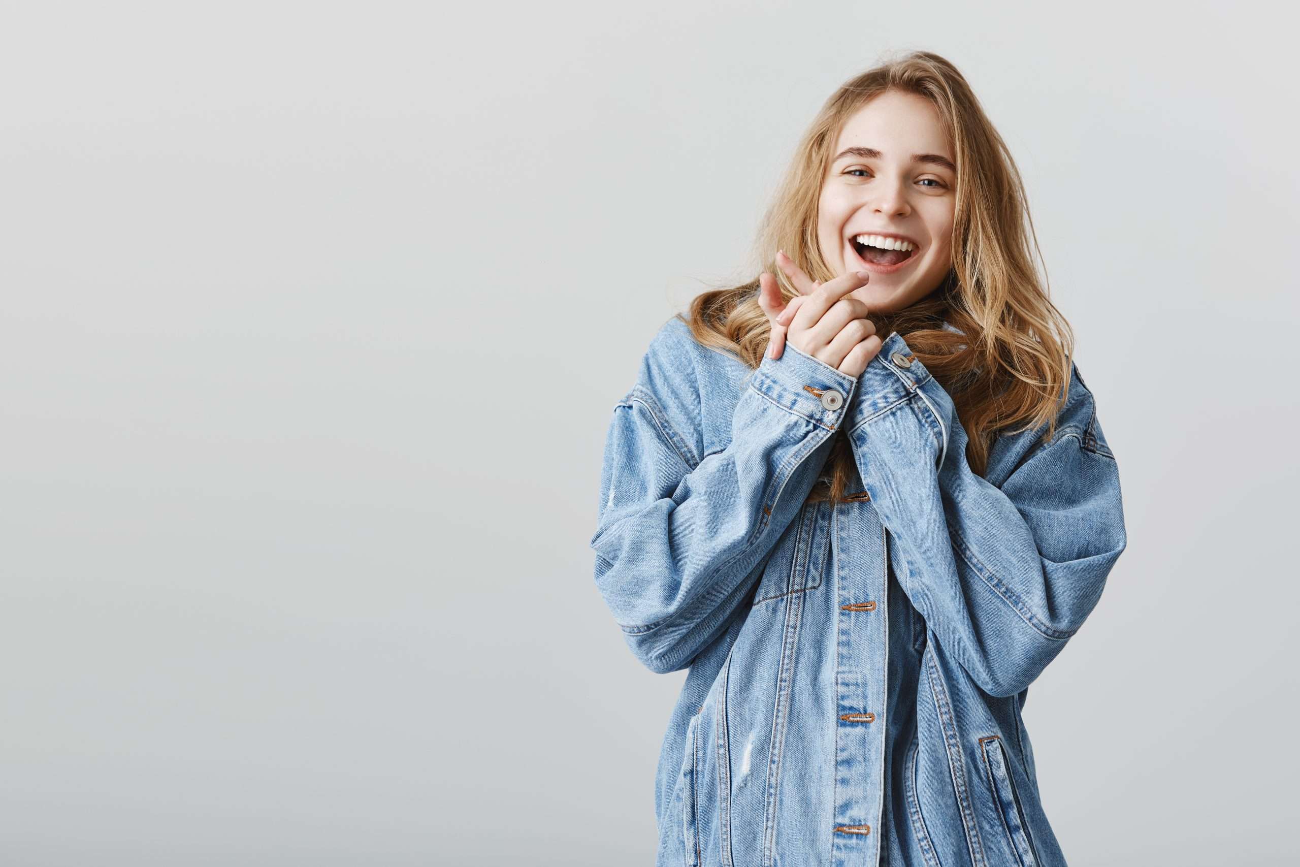 wow, thanks this flowers awesome. portrait of touched pleased young woman with blond hair clasping palms near chest and smiling with satisfaction, being happy to receive moving present over gray wall