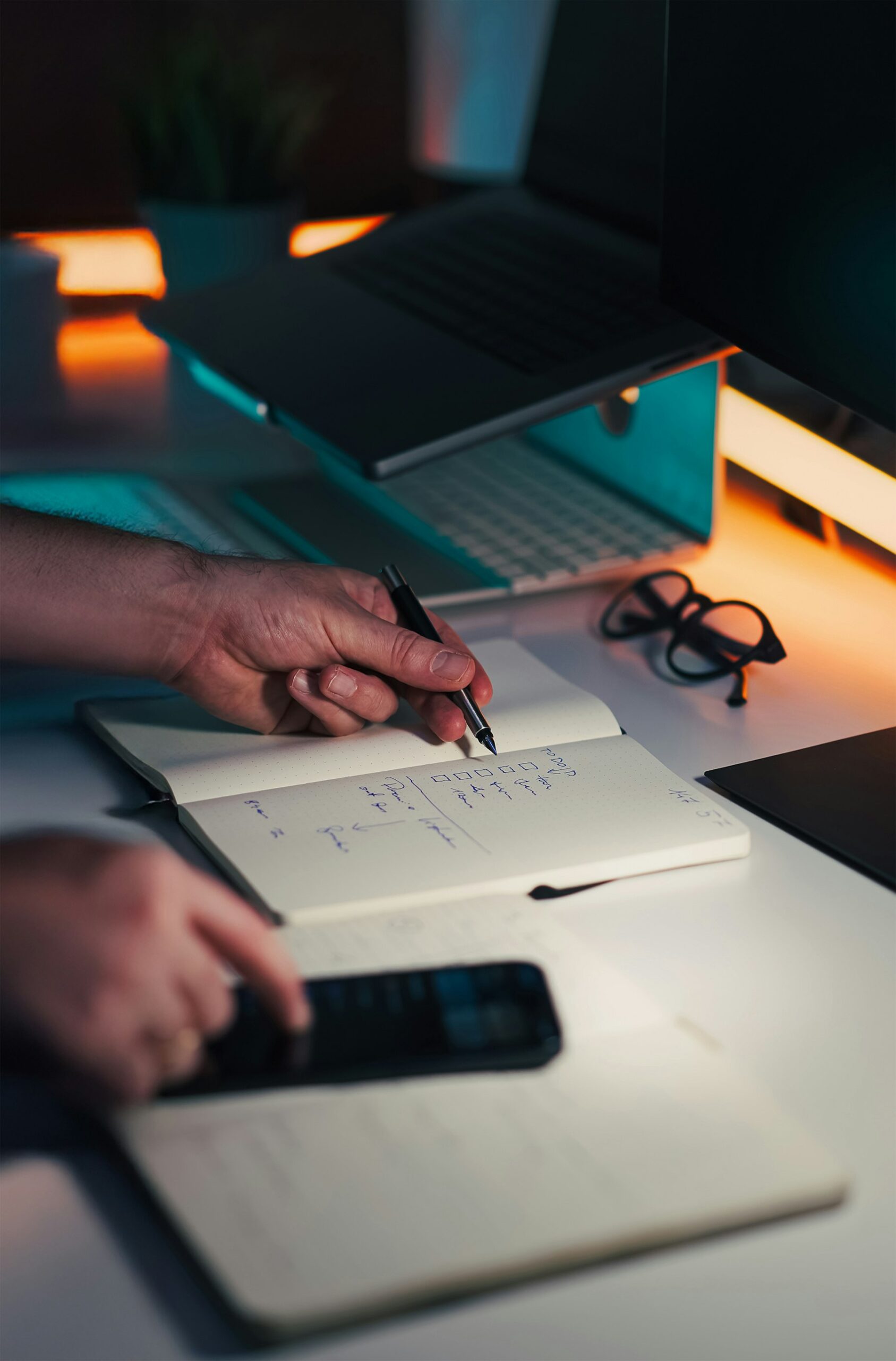 Hands writing a checklist near a laptop, representing a practical next step.